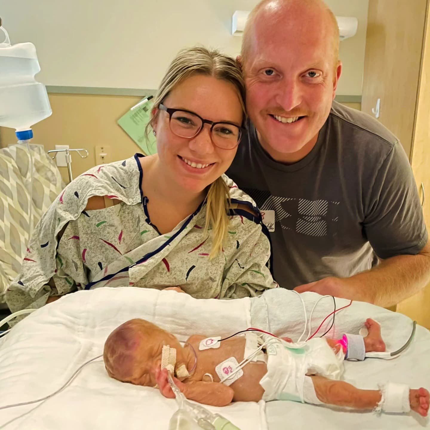 Lincoln in his NICU bed with his smiling mom and dad leaning in beside him