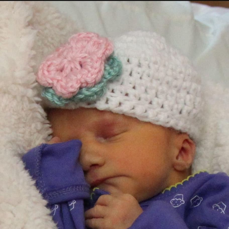 Baby Violet sleeping in a white crocheted hat with a pink and teal flower