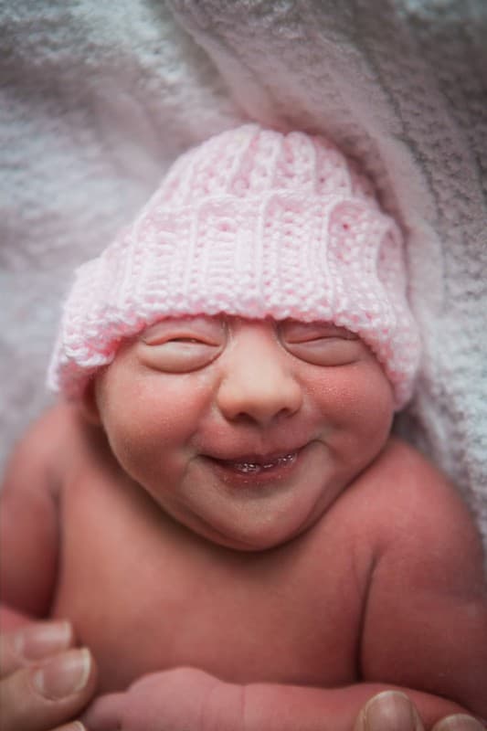 Newborn Ella Marie smiling in her sleep, wearing a pink knitted hat