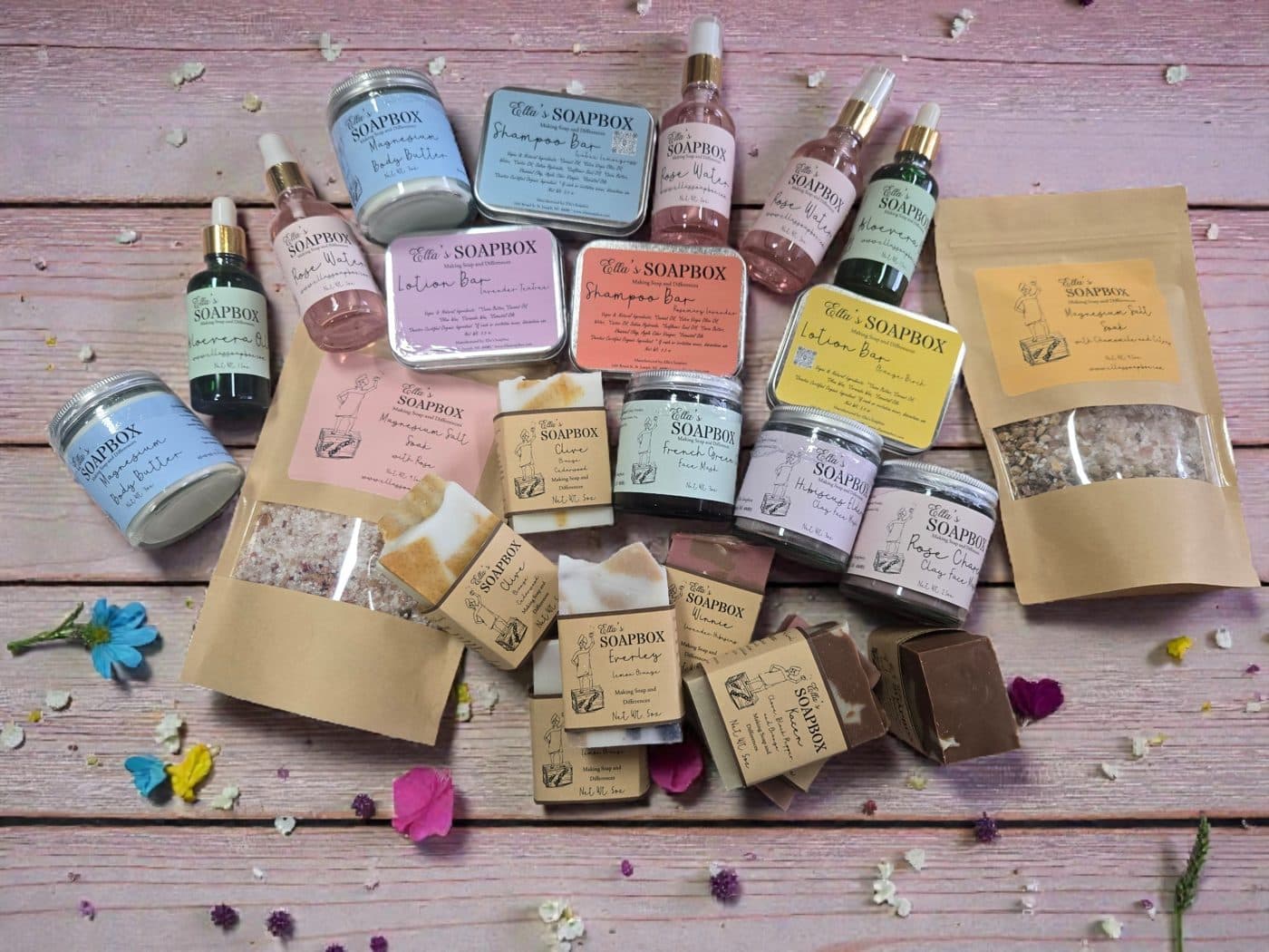 Ella's Soapbox soaps, salts, clay masks and body butters laid out on a pink wooden table