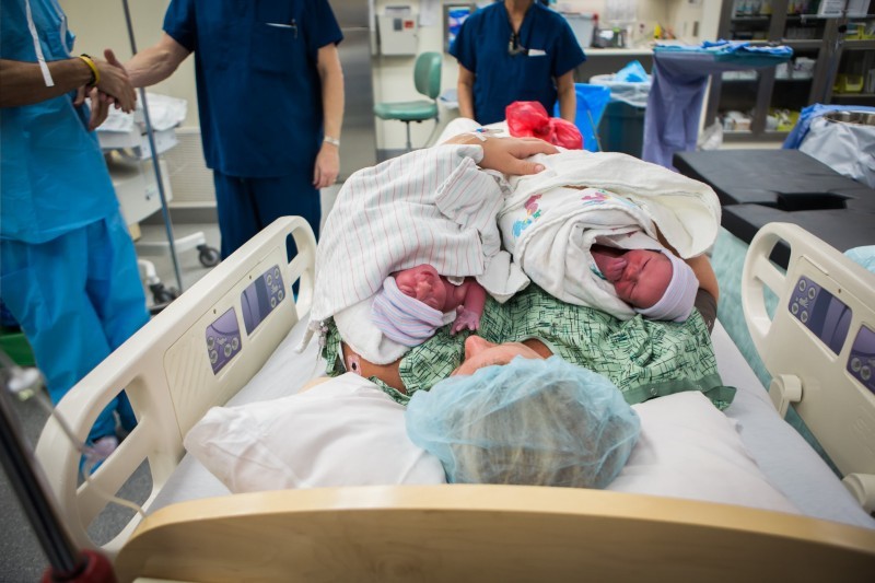 Newborn Lennox and Ella lying together on Erin in the operating room as hospital staff shake hands