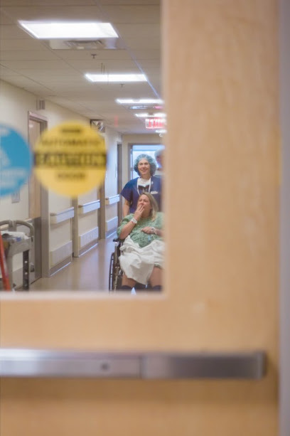 Erin being wheeled down the hospital hallway toward C-Section Room 1, seen through the door window